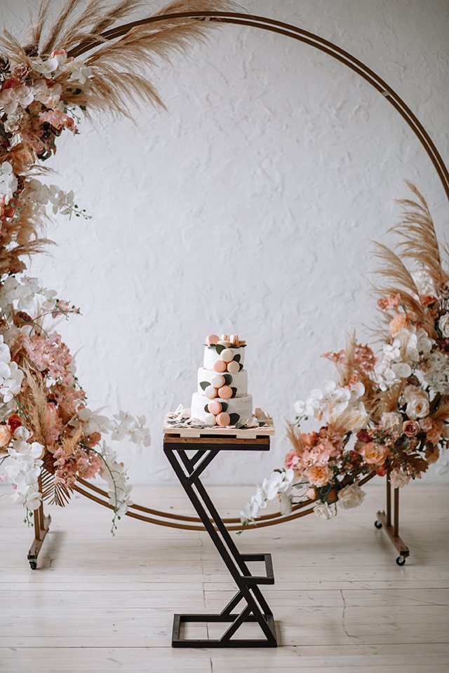 Three-tiered wedding cake on a stand on the background of the arch